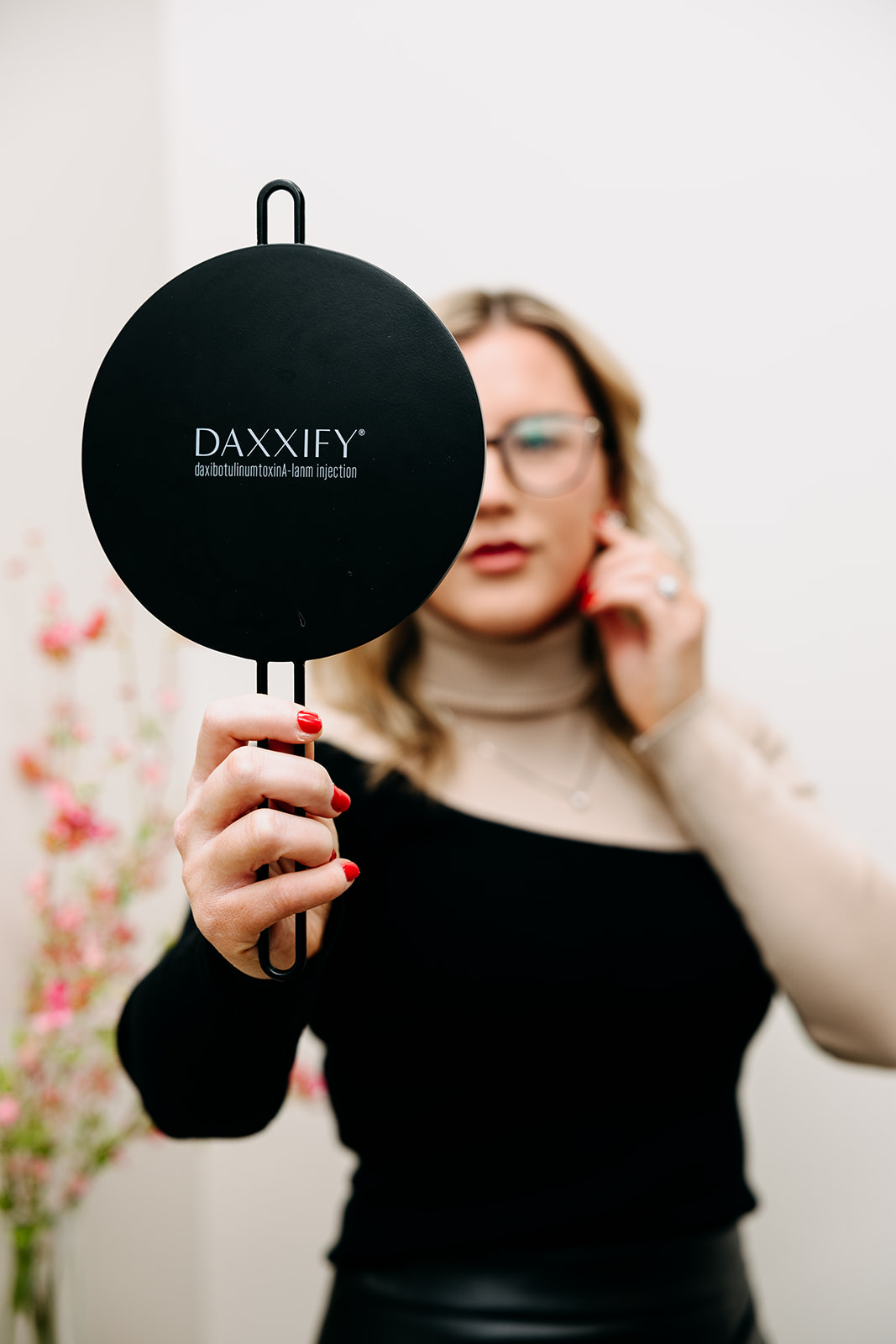 Person holding a round Daxxify sign with blurred flowers in the background.