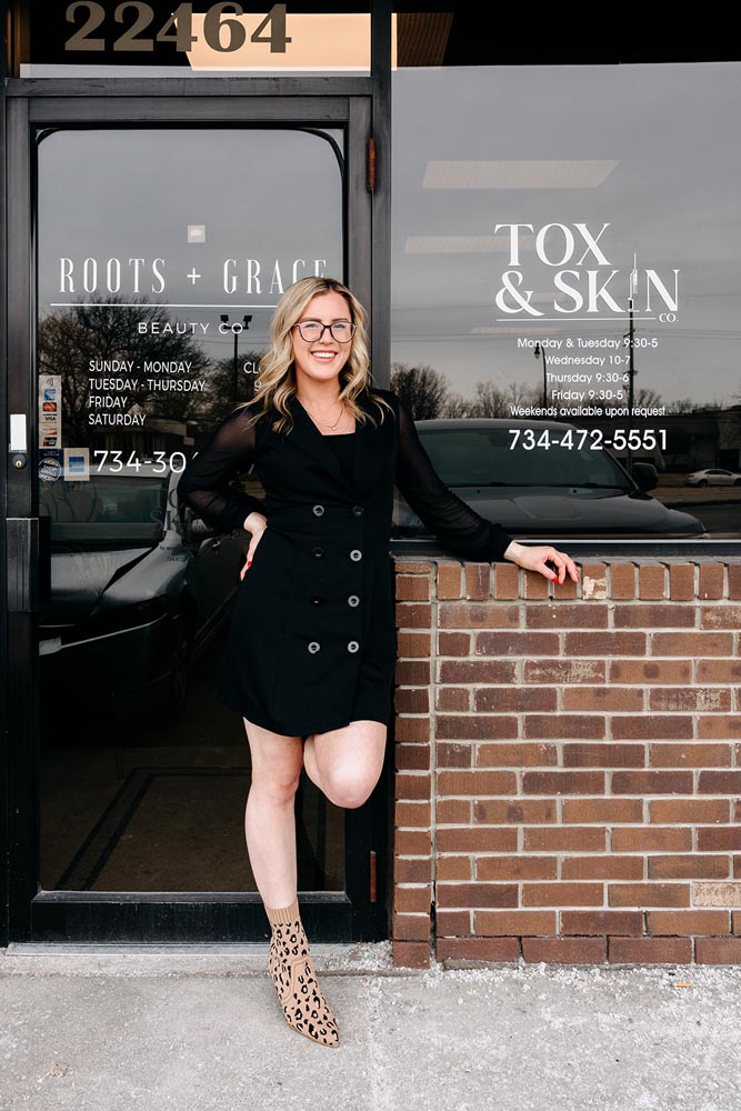 A woman in a black dress and leopard print boots stands outside a beauty shop.