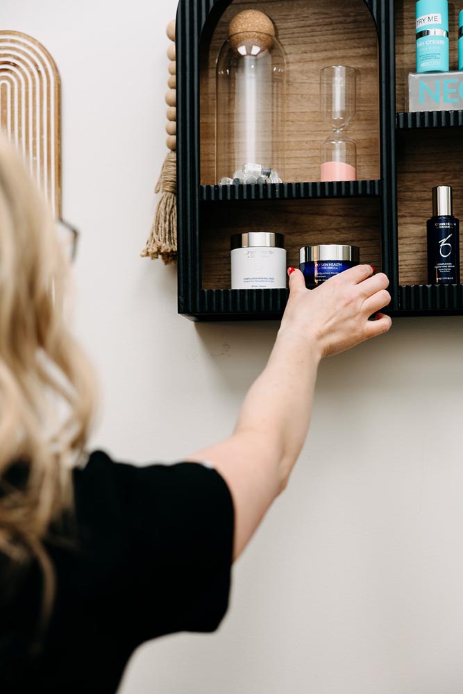 A woman reaching for a jar on a wooden shelf with beauty products.