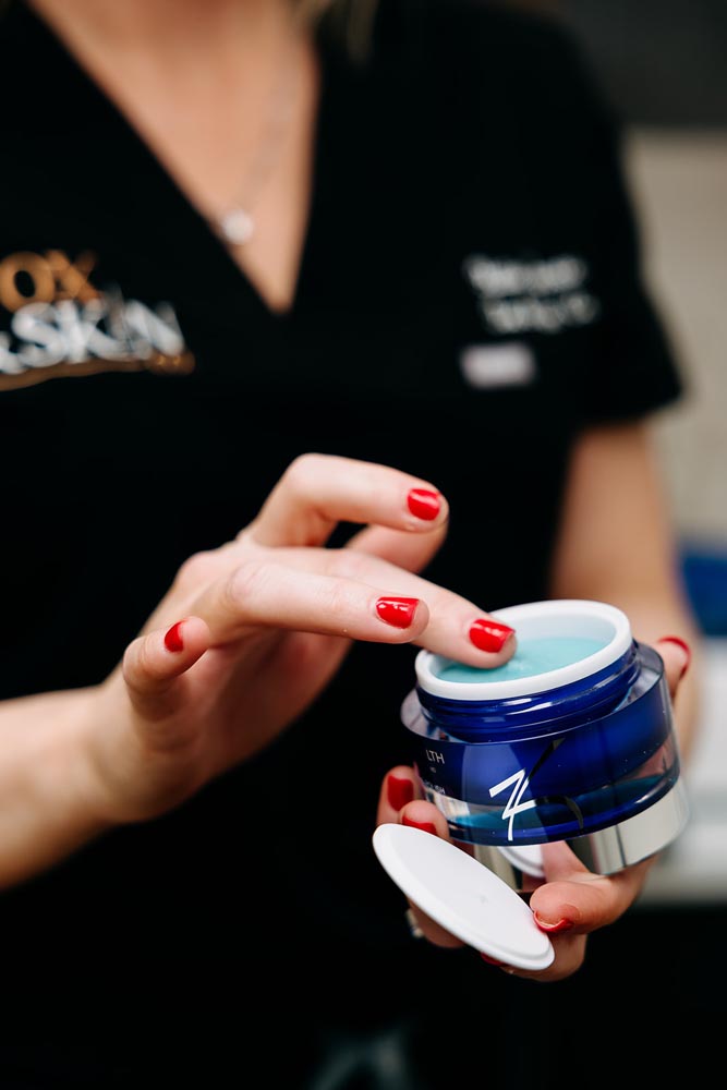 A person applying cream from a blue container with red painted nails.