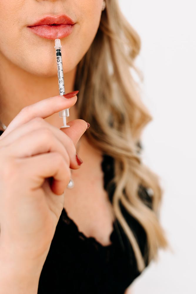 Woman holding a syringe near lips, contemplating beauty treatment.