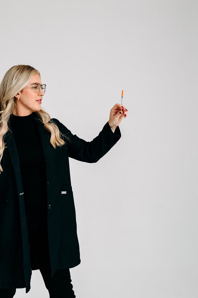 A woman in a black outfit holding an orange-tipped pen against a plain background.