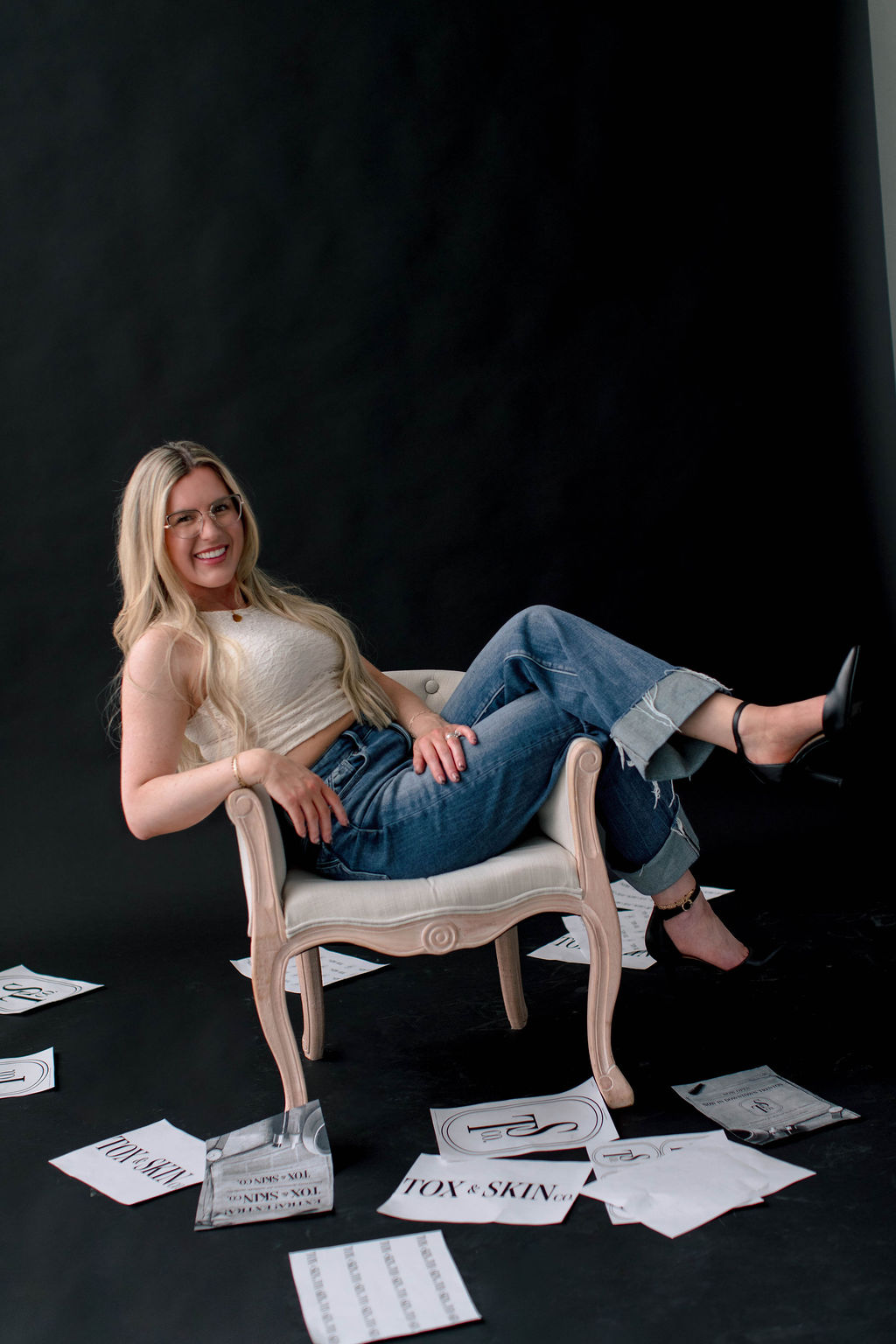 A woman sitting on a chair, surrounded by papers on a dark background.