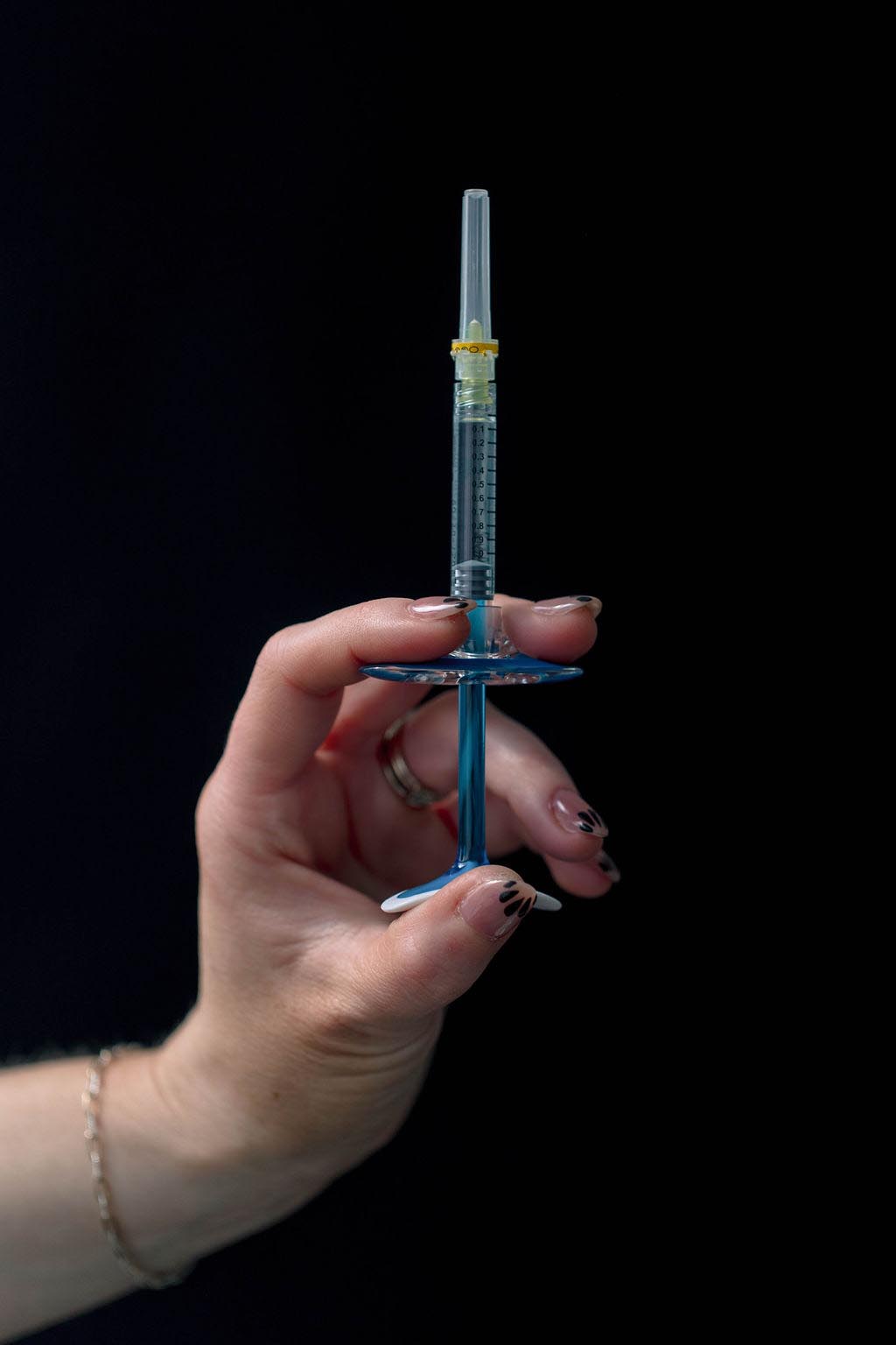 Hand holding syringe against dark background.