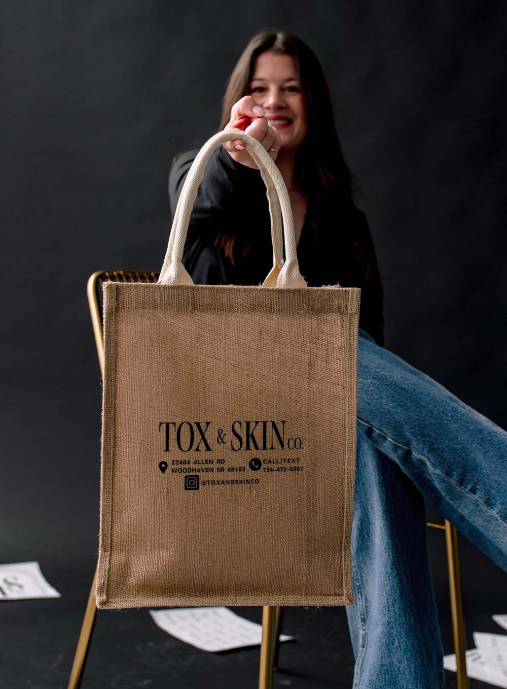 A woman smiling and holding a Tox & Skin Co. branded tote bag.