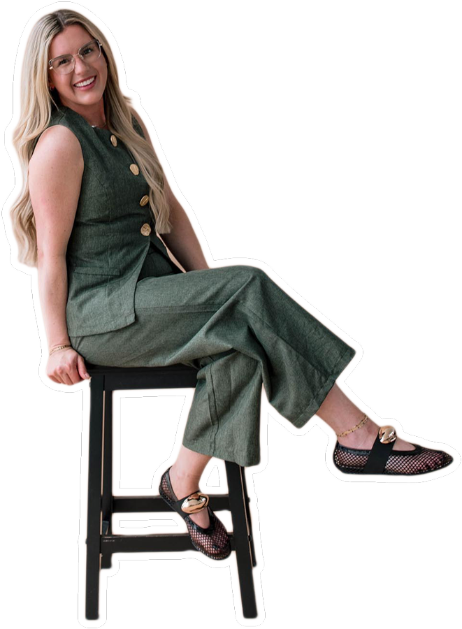 A woman in a green outfit sitting on a stool, smiling and posing.