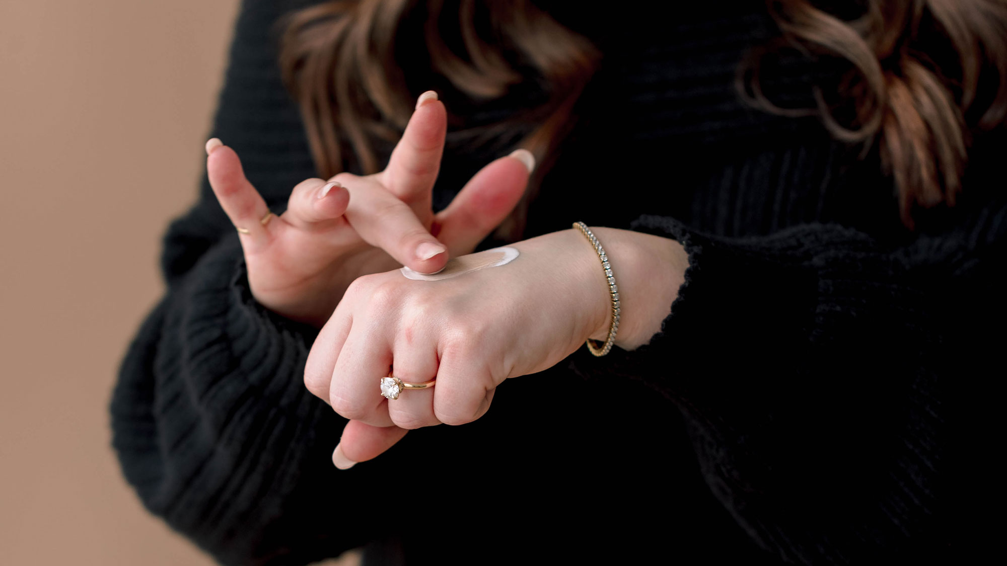 Person applying cream to hand, wearing a ring and bracelet.