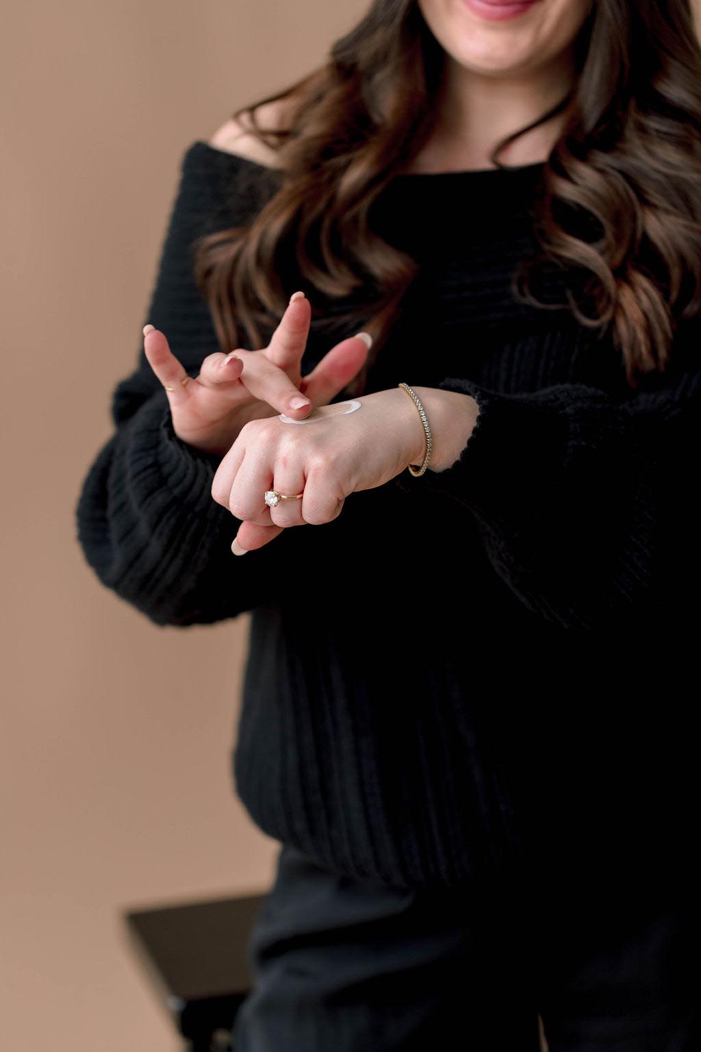 A woman applying cream on her hand while wearing a black sweater.