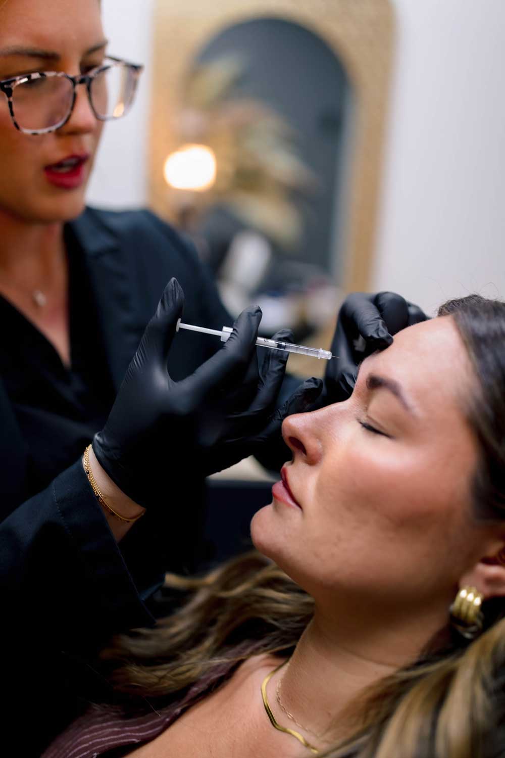 Aesthetician giving facial injection to woman in clinic.