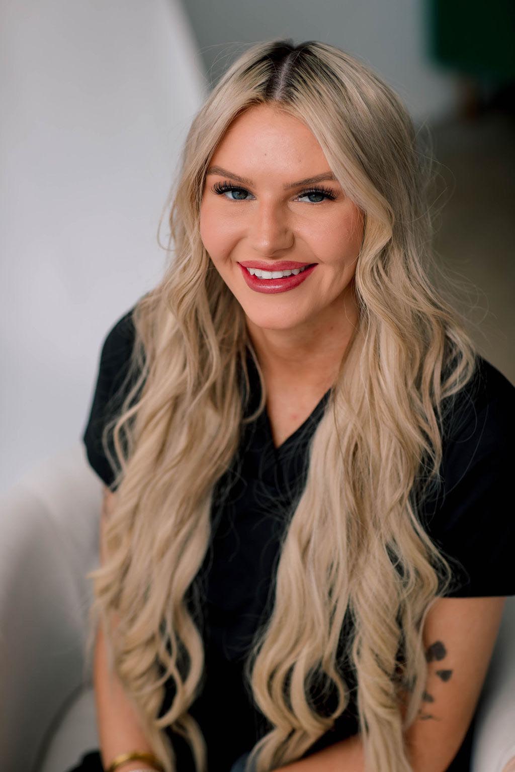 A woman with long blonde hair and a black top smiling at the camera.