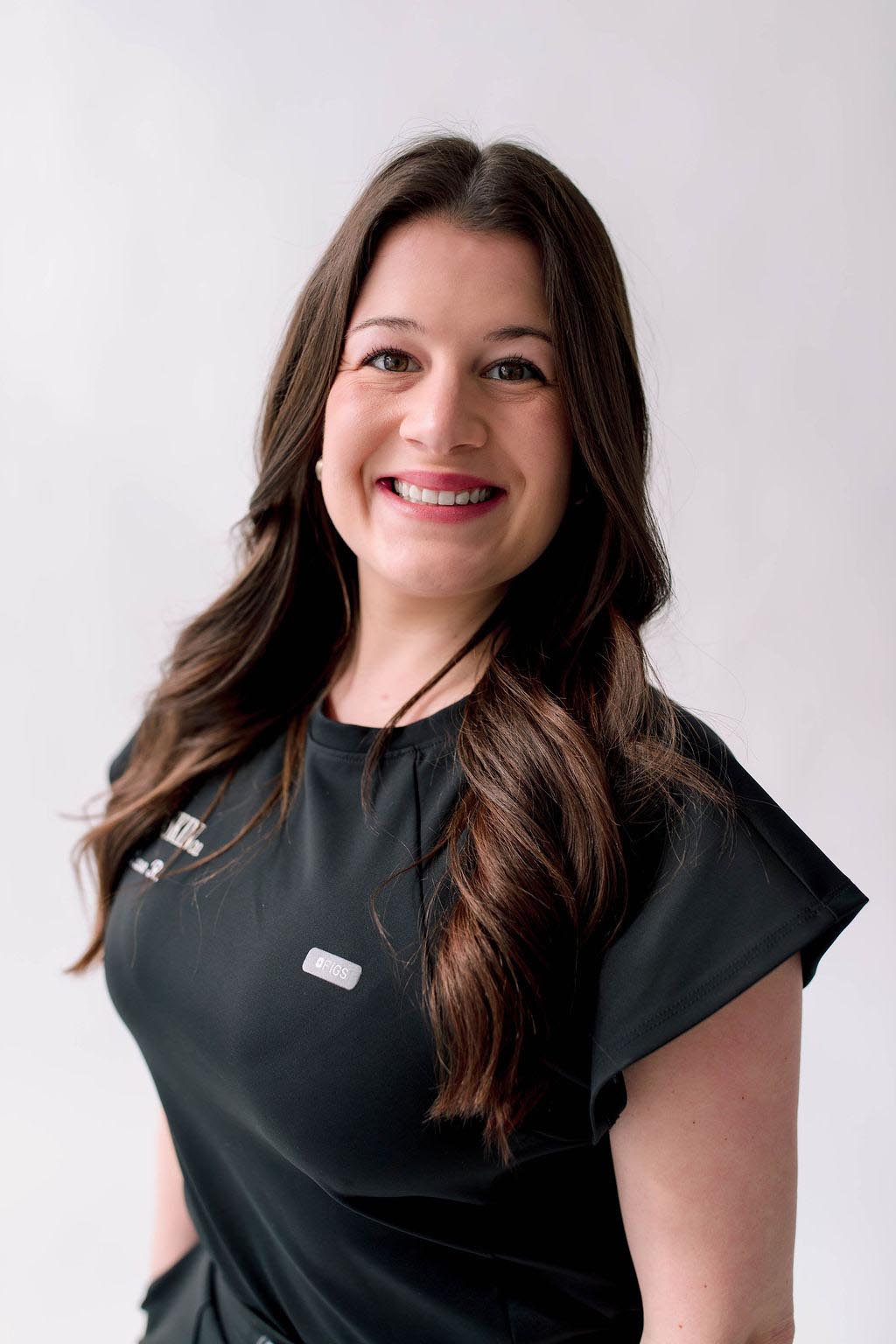 A woman with long brown hair smiling in a black top against a white background.