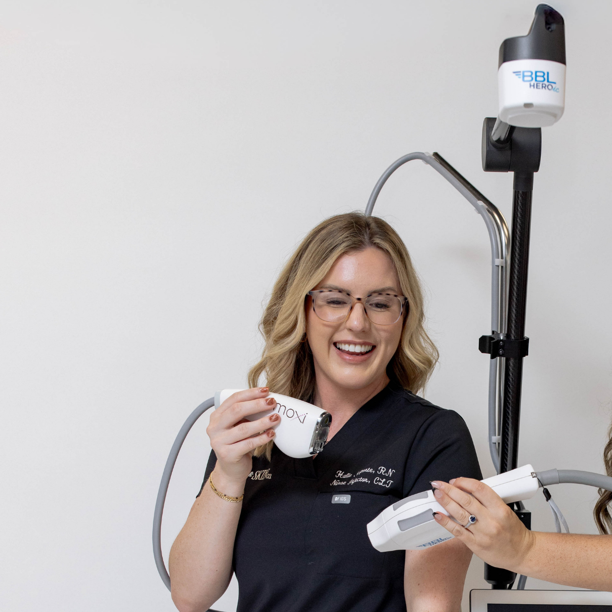 A woman holding a BBL HERO device, smiling during a cosmetic procedure demonstration.