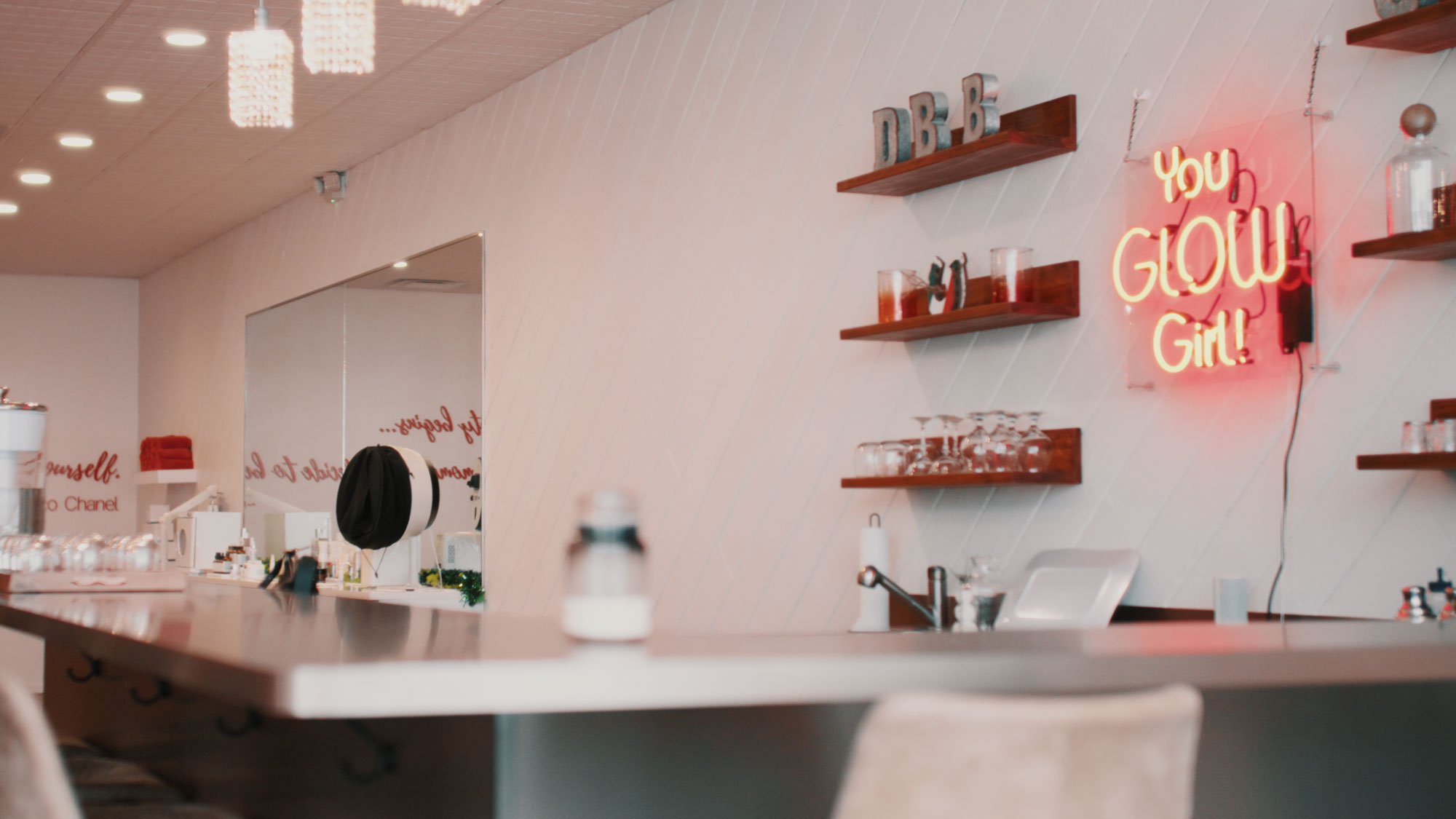Modern cafe interior with a neon sign reading You Glow Girl on wooden shelves.