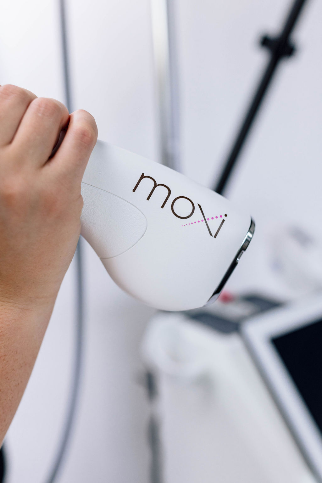 Hand holding Moxi laser device for skin treatment in a clinic setting.