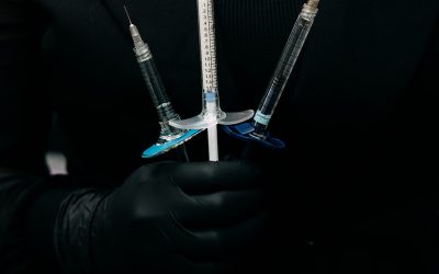 Person in black glove holding three syringes in a black outfit.