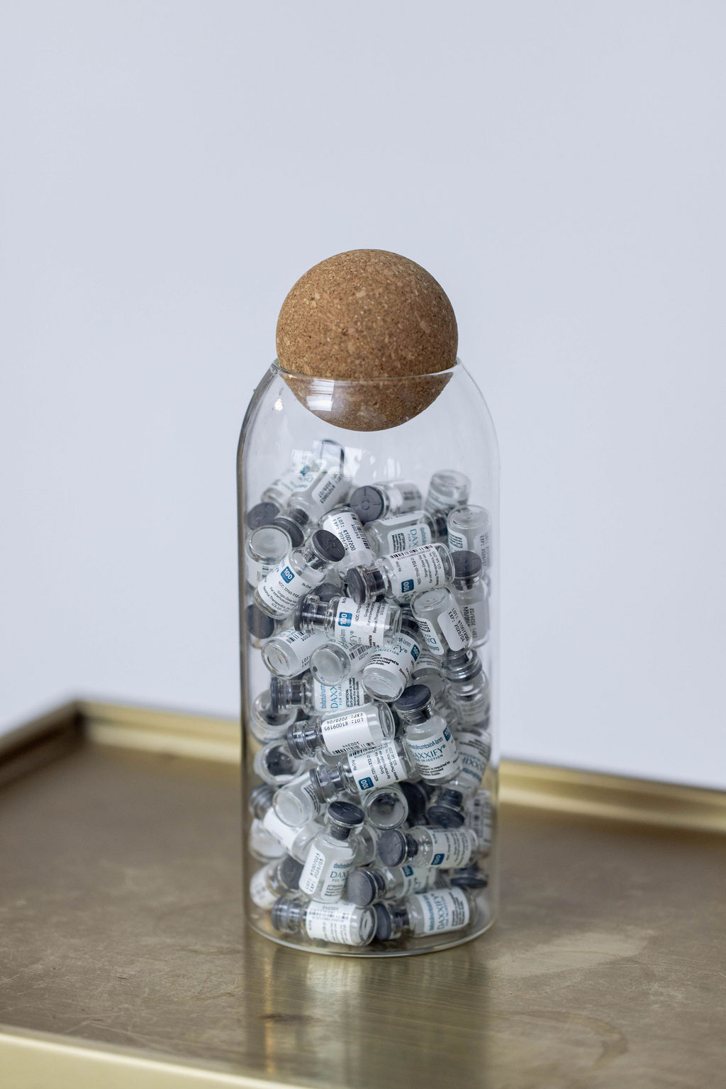 Glass jar filled with small vials, sealed with a cork lid, on a wooden surface.