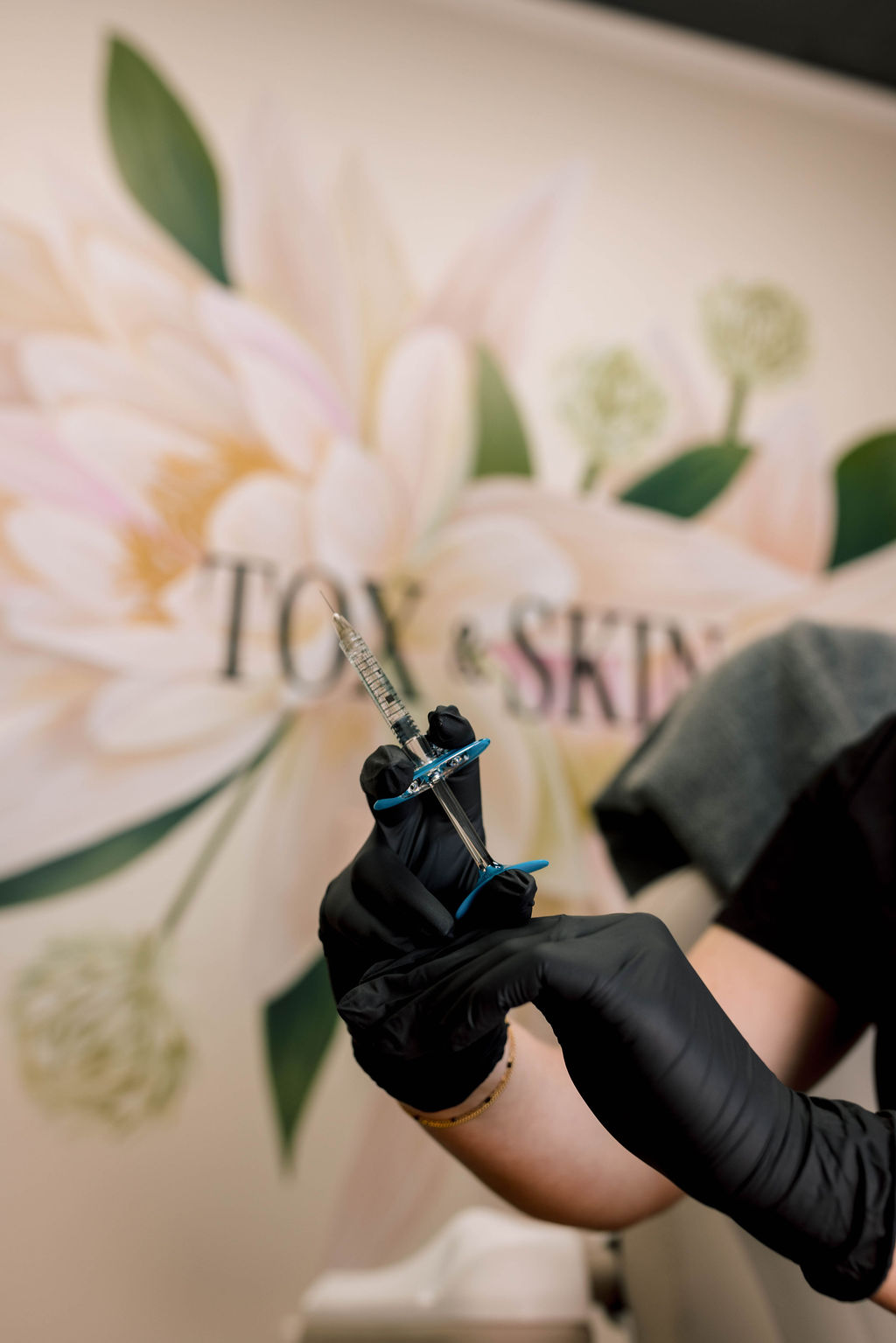 Black-gloved hands holding a syringe in a skincare clinic.