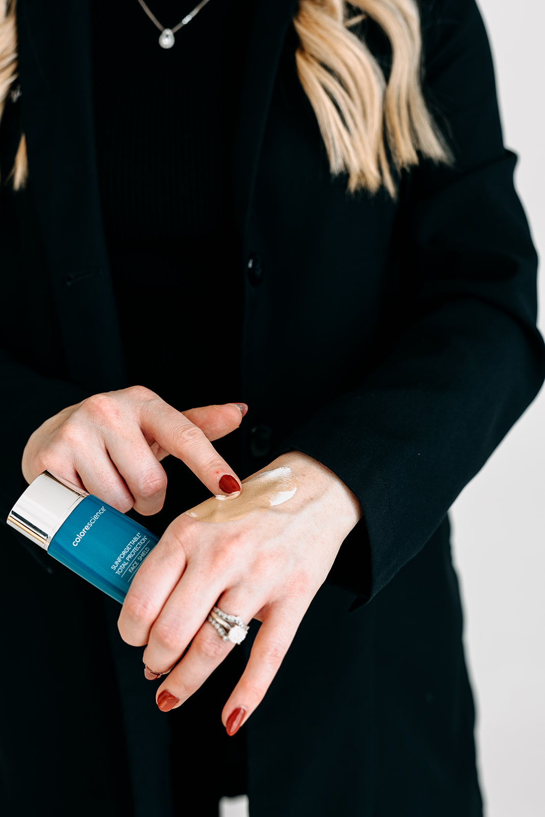 A person applying SPF cream from a Colorescience bottle onto their hand.