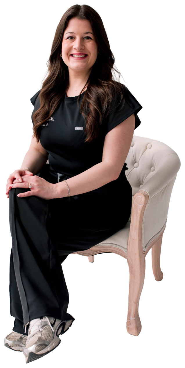 A woman sitting on a chair, wearing black attire and sneakers, smiling at the camera.