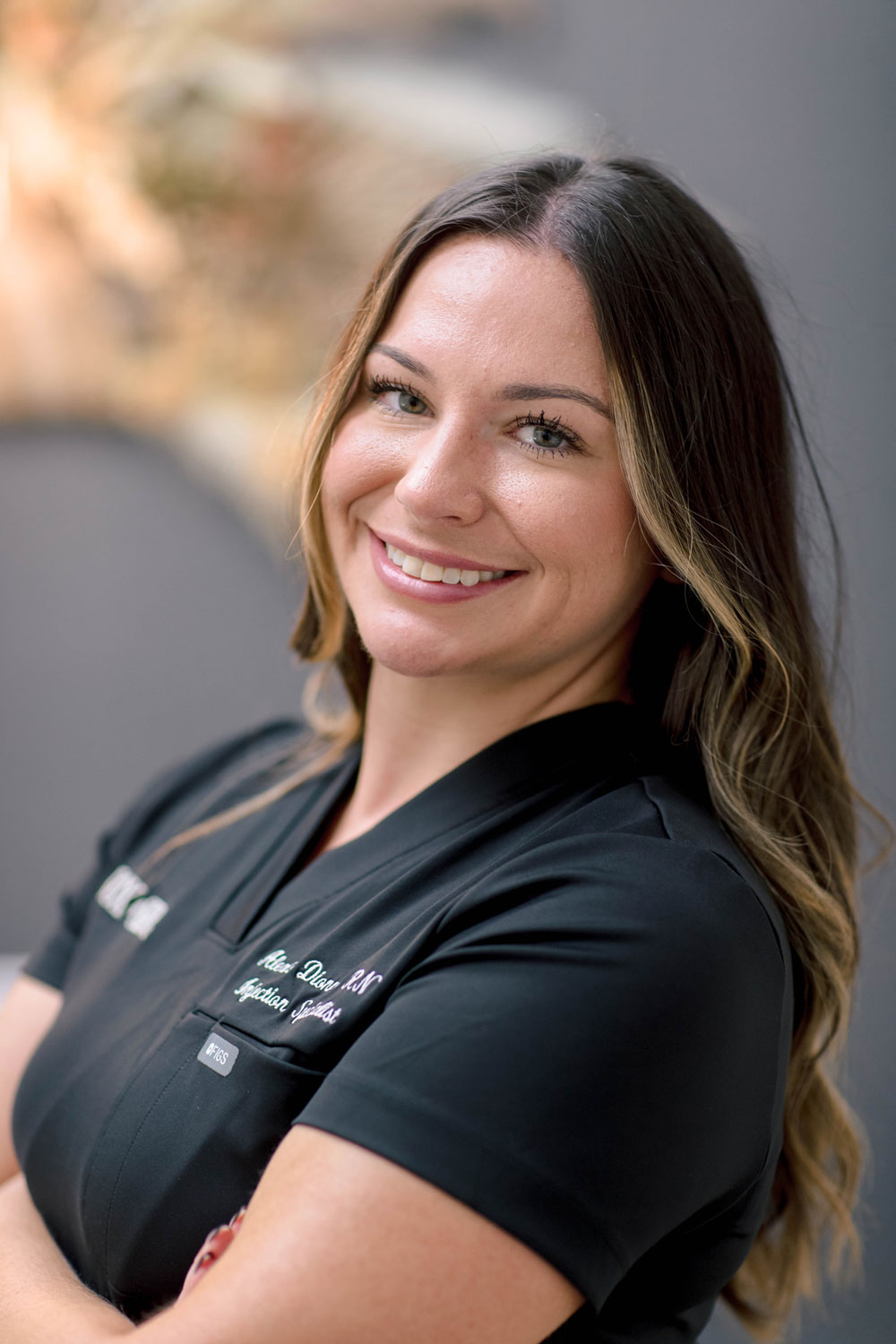 A woman in a black uniform smiles confidently, with blurred background.