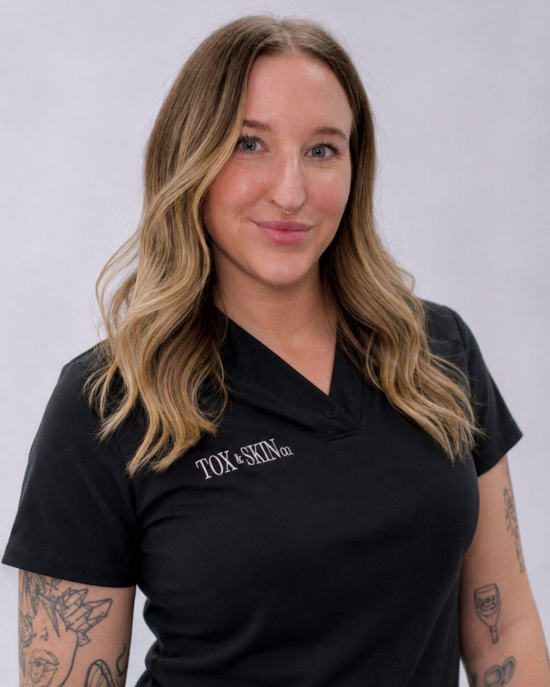 A woman with long hair in a black shirt with Tox & Skin logo, smiling.