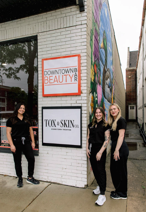 Three women standing outside Downtown Beauty Bar and Tox & Skin Co. with a mural on the building.